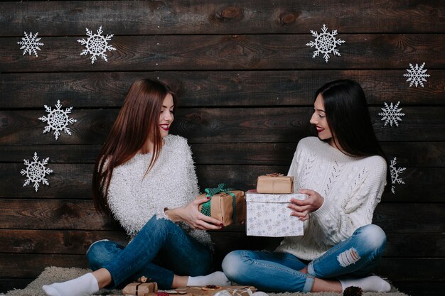 Two pretty young funny women friends smiling and give each other gifts