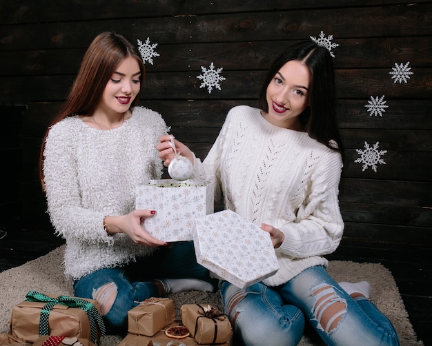 Due amici di donne divertenti abbastanza giovani sorridenti e divertendosi, che tengono i regali di festa, pronti per la celebrazione.