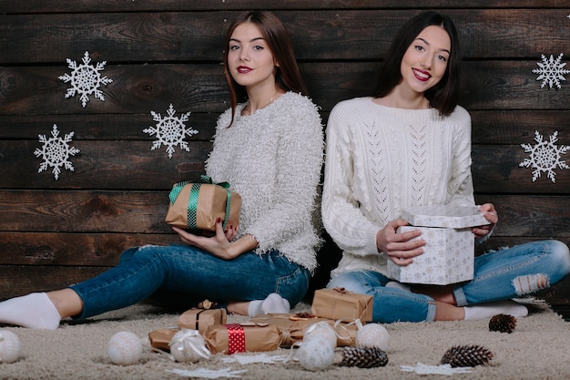 Due amici donne divertenti abbastanza giovani che sorridono e che si divertono, che tengono i regali di festa