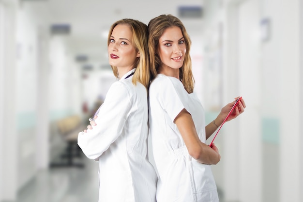 Two pretty young women doctors, nurses standing back to back in the hospital.