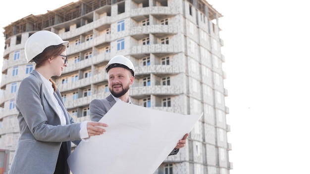 Two professional smiling engineering holding blueprint and looking at each other