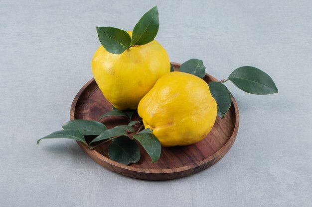 Two quinces with leaves on wooden plate