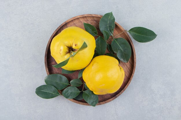 Two quinces with leaves on wooden plate