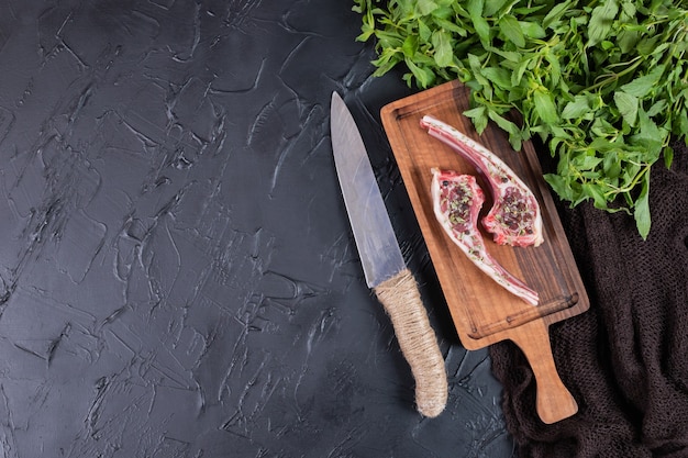 Two raw beef chops on wooden board with fresh mint and knife.