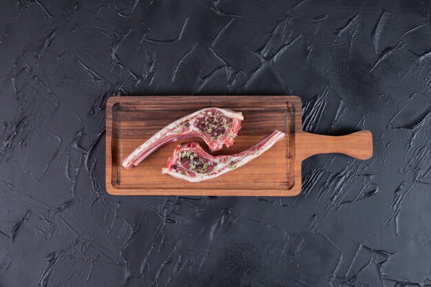 Two raw beef chops on wooden board.