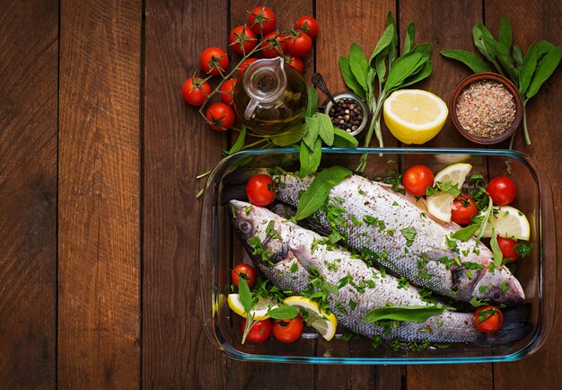 Two raw seabass in a baking dish with spices on an old wooden table. Top view