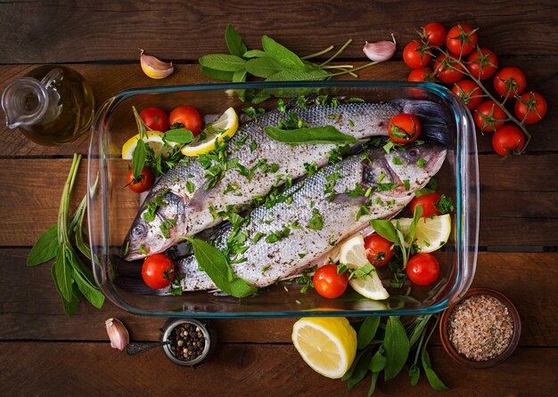 Two raw seabass in a baking dish with spices on an old wooden table. Top view