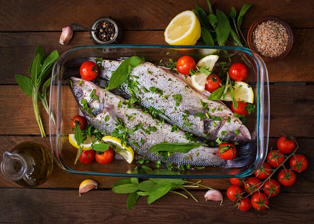 Two raw seabass in a baking dish with spices on an old wooden table. Top view