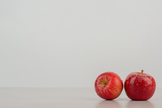 Two red apples on marble table .