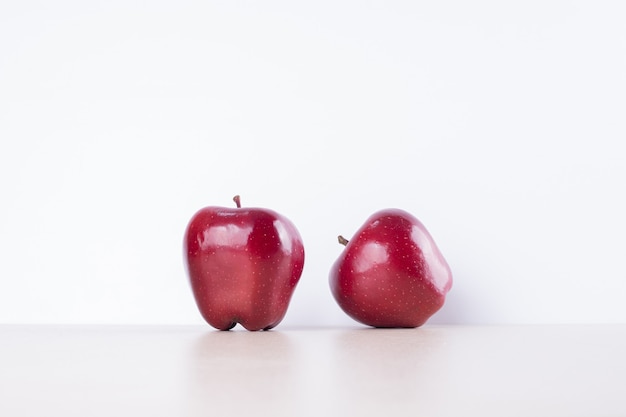 Two red apples on white surface .