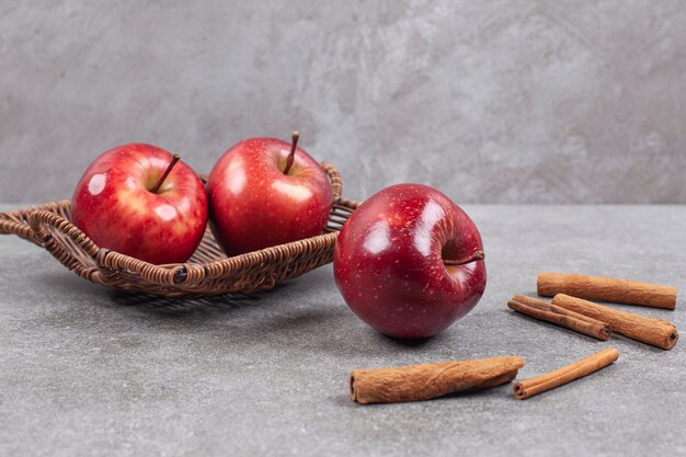 Two red apples in wooden basket with cinnamon sticks