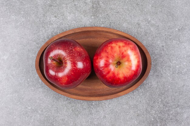 Two red apples on wooden plate