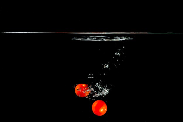 Two red tomatoes falling in water against black background