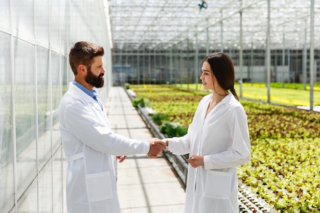 Two researchers in laboratory robes walk around the greenhouse and shake each other hands