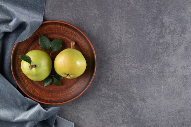 Two ripe pear on a plate and pieces of fabric, on the blue table.