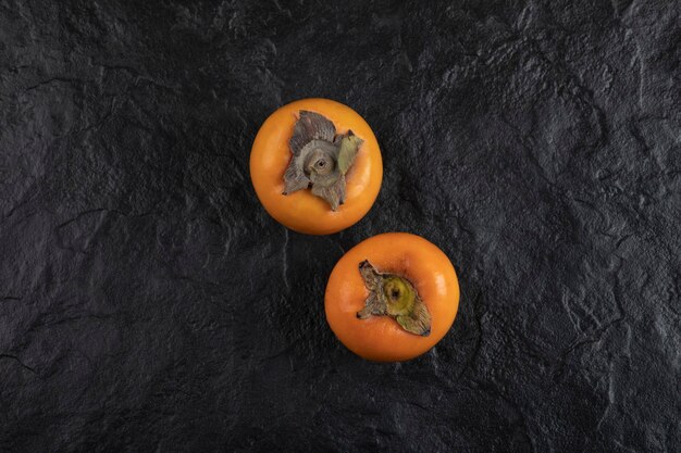 Two ripe persimmon fruit placed on black surface