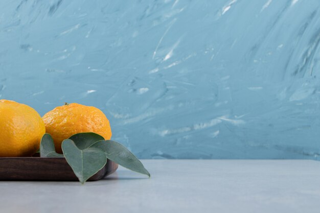 Two ripe tangerines with leaves on dark plate