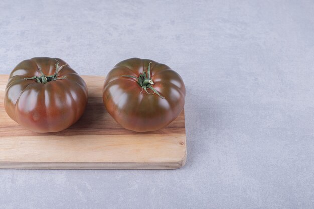 Two ripe tomatoes on wooden board.