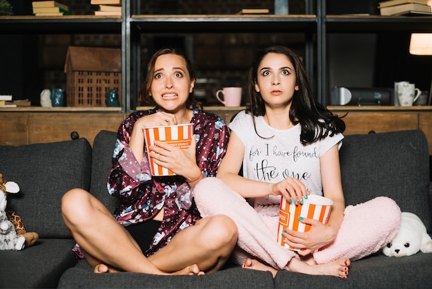 Two scared female friends watching horror movie