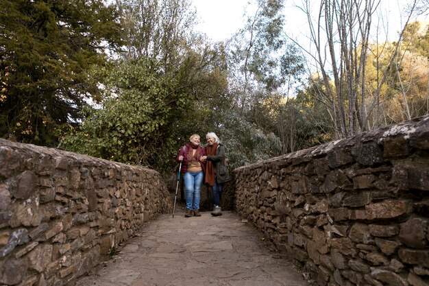 Two senior women crossing a stone bridge while out in nature