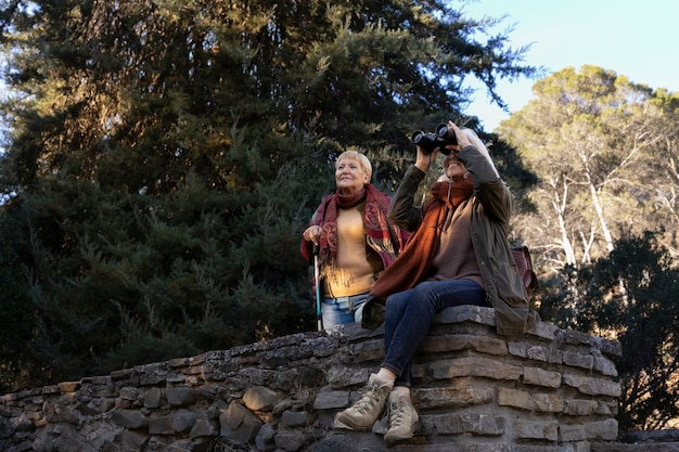쌍안경을 사용하면서 자연에서 하이킹을 즐기는 두 노인 여성