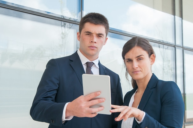 Two serious coworkers using tablet during outdoor work break