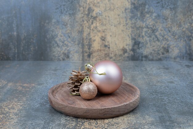 Two shiny Christmas balls with one pinecone on wooden plate