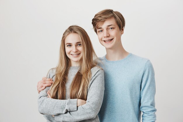 Two siblings smiling at camera. Sister and brother with braces hugging