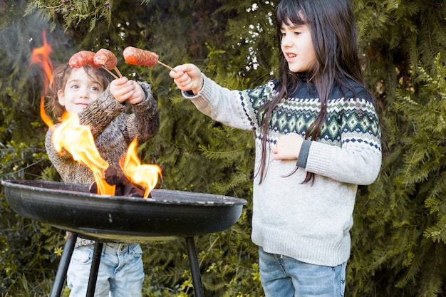 Two sisters cooking sausages on portable barbecue