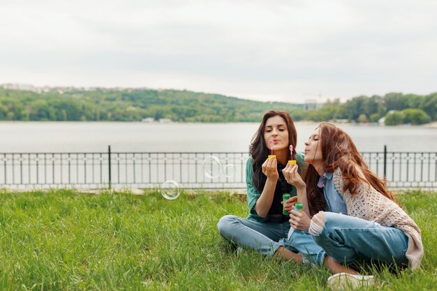 Two sisters having fun while making bubbles and sitting on the grass