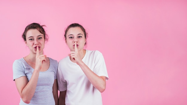 Two sisters making quiet gesture against pink backdrop