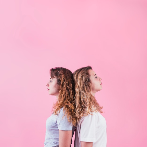 Free photo two sisters standing back to back against pink backdrop