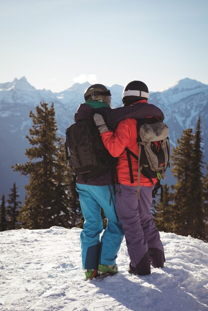 Two skiers standing together with arm around on snow covered mountain