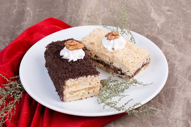 Two slices of cakes on white plate with red tablecloth.