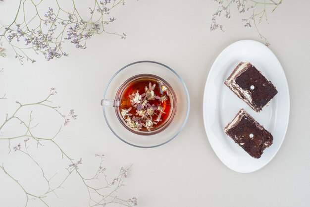 Two slices of tiramisu cake and cup of tea on white surface