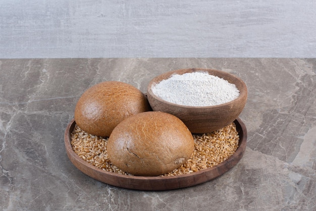 Due piccoli panini e una ciotola di farina su un vassoio su fondo marmo. foto di alta qualità