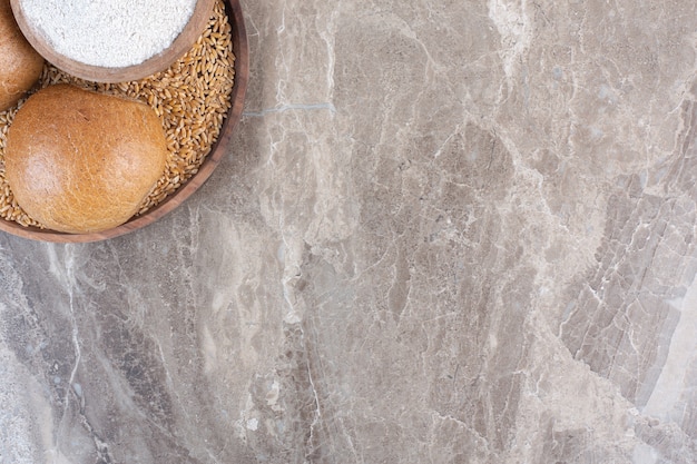 Two small buns and a bowl of flour on a tray on marble.