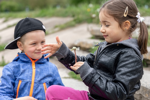 Two small children are playing with dandelions on a walk