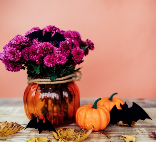 Две маленькие декоративные тыквы и ваза с хризантемами, бумажные летучие мыши на столе. подготовка к празднику хэллоуина.