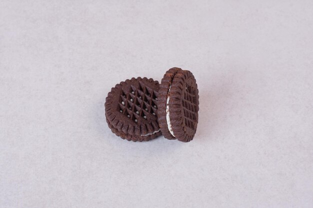 Two, small, sweet chocolate cookies on white table.