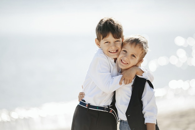 Two smiled brothers are hugging each other near the sea and looking straight