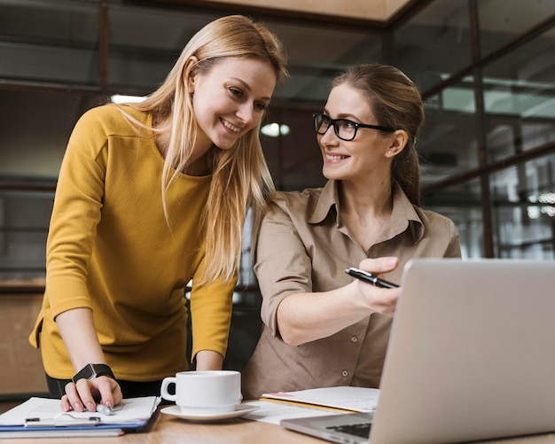 Two smiley businesswomen working with laptop at desk