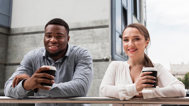 Два улыбающихся коллеги вместе пьют кофе на работе во время пандемии