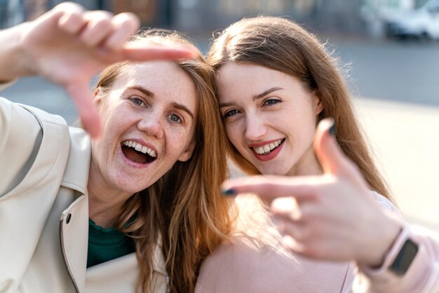 Two smiley female friends outdoors in the city pretending to take a selfie