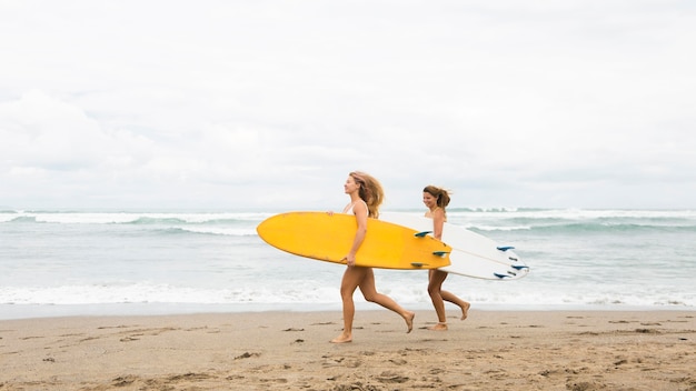 Two smiley friends running on the beach with surfboards and copy space