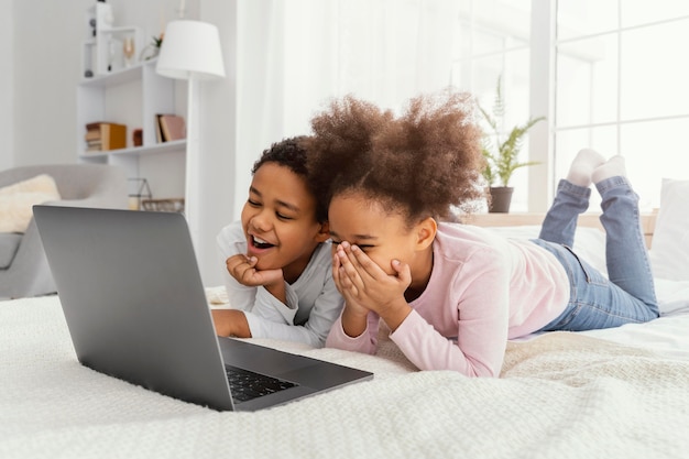 Two smiley siblings at home together playing on laptop