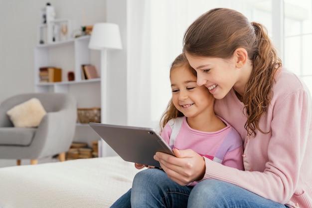 Two smiley sisters together at home using tablet