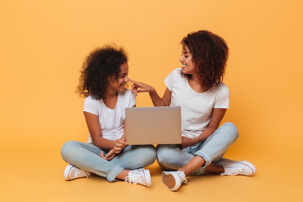 Two smiling afro american sisters holding laptop computer