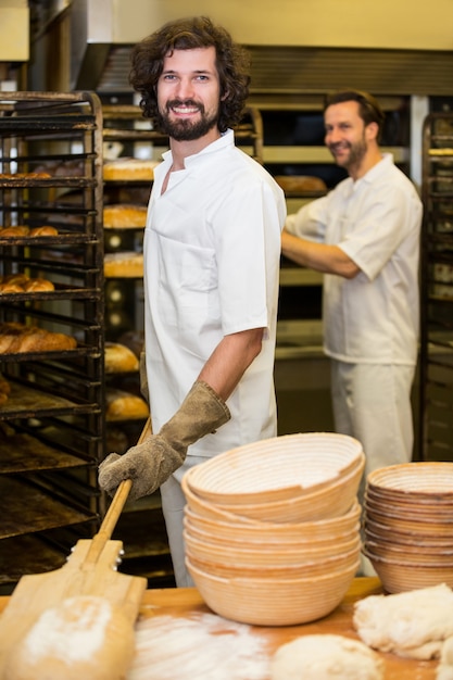 Two smiling bakers preparing bread in bakery kitchen