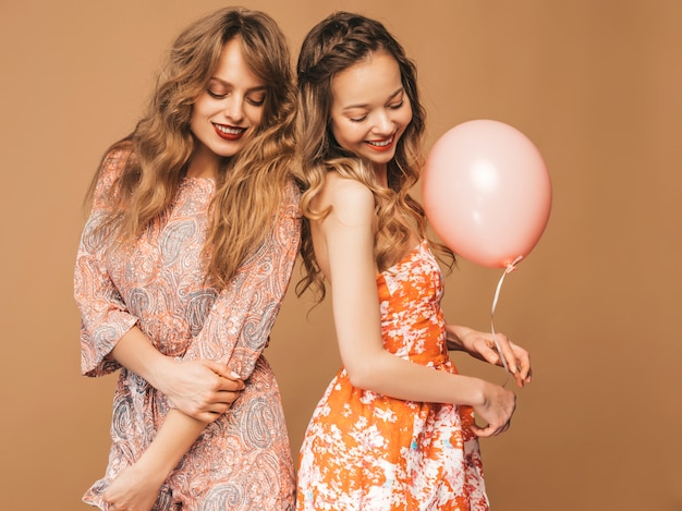 Foto gratuita due belle donne sorridenti in abiti estivi. ragazze in posa modelli con palloncini colorati. divertirsi, pronti per la festa di compleanno o festa